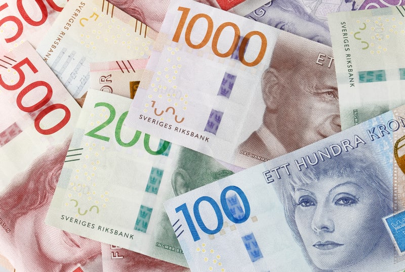 Bilden visar en närbild uppifrån på flera svenska sedlar utspridda över en yta. Sedlarna är av olika valörer och färger. Tydligt synliga valörer inkluderar 1000 kronor (gul/beige/lila), 500 kronor (röd), 200 kronor (grön) och 100 kronor (blå). Texter