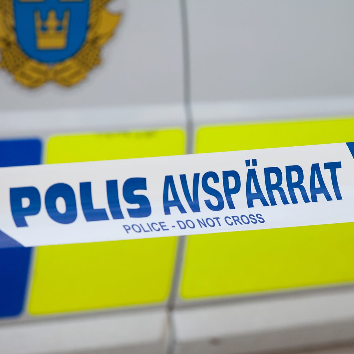 Bilden visar ett närbildsfoto av en avspärrningstejp. Tejpen är vit med en blå rand längs över- och underkanten. På tejpen står texten "POLIS AVSPÄRRAT" i stora blå bokstäver. Under den svenska texten står det "POLICE - DO NOT CROSS" i mindre blå bok