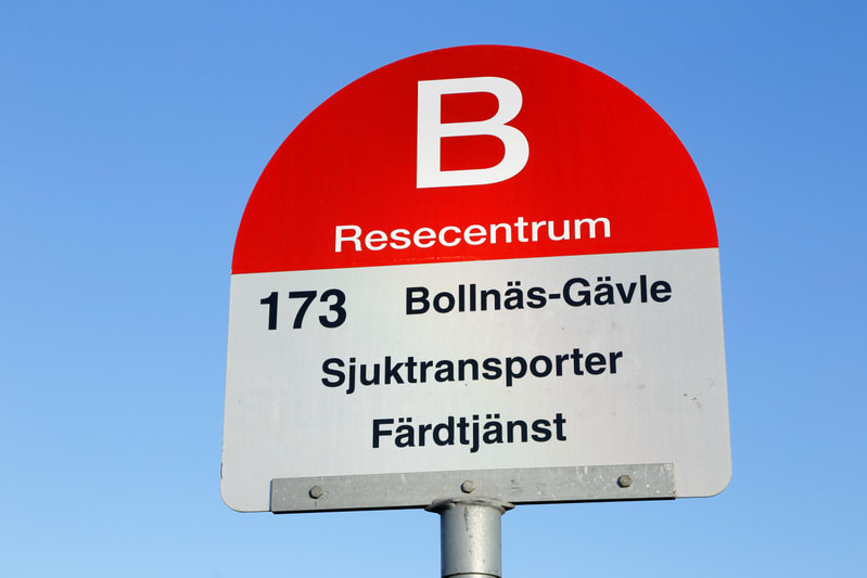 Bilden visar en närbild av en skylt för kollektivtrafik, monterad på en metallstolpe. Skylten är röd och vit med svart text. Den övre halvcirkelformade delen är röd med ett stort vitt 'B' centrerat. Under 'B' står texten 'Resecentrum' i vitt. Den ned