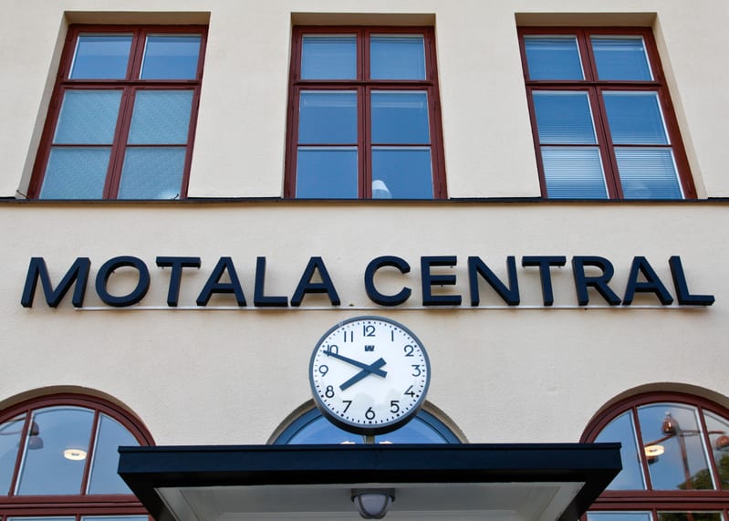 En fasad på en byggnad med det svarta texten "MOTALA CENTRAL" på en ljusbeige yta. Ovanför texten finns tre fönster med bruna ramar och under texten, centrerat, sitter ett runt ur med vita urtavlor, svarta siffror och visare, som visar tiden runt kva