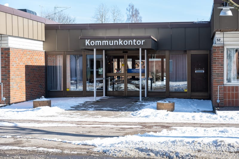 En byggnad med tegelväggar och ett brunt tak i dagsljus. Ovanför entrén står texten "Kommunkontor". Markytan framför är täckt med snö. Ett par träd syns i bakgrunden. Nummer 52 syns på fasaden till höger.
