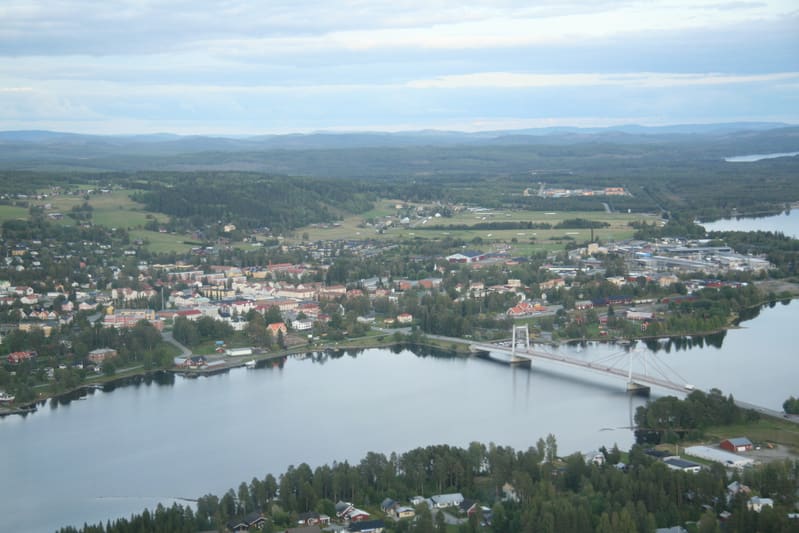 En vidvinkelbild tagen uppifrån över ett landskap som innefattar en stadskärna, en bro, vattendrag och skogsområden. Vattendraget delar bilden i två större landytor. Längre bort syns blåa kullar.