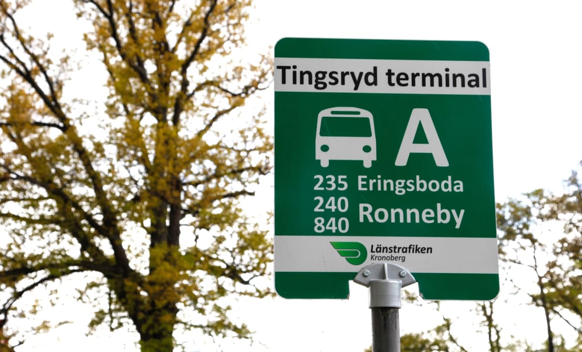 En bild av en grön busshållplatsskylt som visar "Tingsryd terminal" och busslinjerna 235 Erlingsboda, 240 Ronneby och 840. Logotypen för Länstrafiken Kronoberg finns nedtill. I bakgrunden syns ett träd med gulgröna löv mot en ljus himmel.
