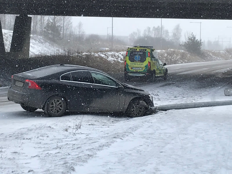 Bilden visar en kollision på en snötäckt väg. En mörk personbil står snett på vägkanten med fronten in i en metallstolpe eller räcke som ligger ned. Hjulen på personbilen är delvis täckta av snö och det syns skador på bilens front. I bakgrunden syns