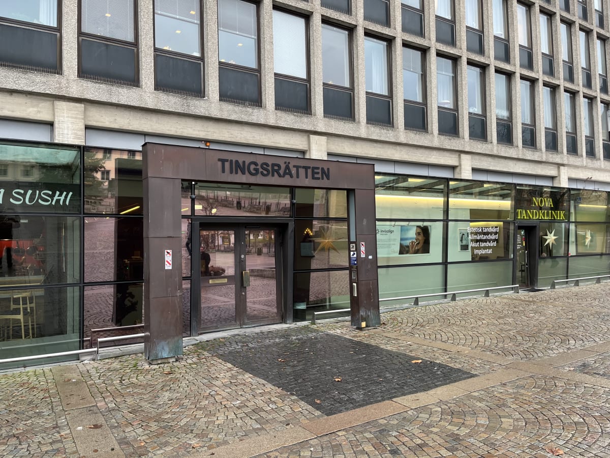 Bilden visar entréerna till en byggnad som inhyser Tingsrätten, en sushirestaurang och en tandklinik. Tingsrättens entré är i mitten, markerad med en skylt där 'TINGSRÄTTEN' står skrivet. Till vänster om tingsrätten syns en del av en sushirestaurang