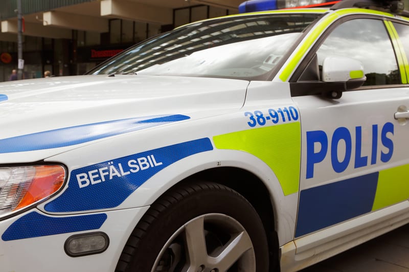 En nära bild visar sidan av en vit svensk polisbil. Bilen har blåa och limegröna reflekterande dekaler. På framskärmen står texten "BEFÄLSBIL" i vitt på en blå bakgrund. Framför dörren finns en kombination av blått och limegrönt, med siffrorna "38-91