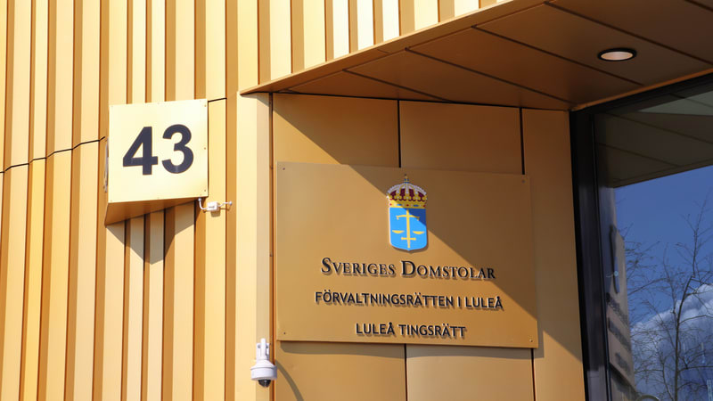 Bilden visar fasaden på en byggnad med gyllene eller beiga paneler. På fasaden syns en kvadratisk skylt med siffran '43' i svart text. Under denna skylt, men på en utskjutande del av byggnaden, sitter en rektangulär skylt med texten 'SVERIGES DOMSTOL
