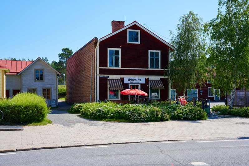 Bilden visar en gata med flera hus i förgrunden och bakgrunden. Ett framträdande rött trähus med vitmålade fönsterramar, vita fönsterkarmar och en röd tegelstensskorsten syns i mitten av bilden. På huset finns en skylt med texten "Bräcke Livs" och tv