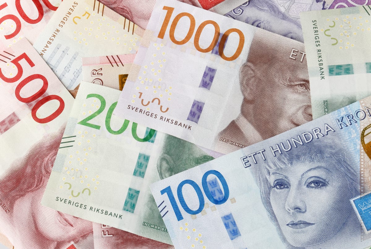Bilden visar ett arrangemang av svenska sedlar i olika valörer, utspridda så att de överlappar varandra. Valörerna som är synliga inkluderar 1000-kronorssedlar, 500-kronorssedlar, 200-kronorssedlar och 100-kronorssedlar. Sedlarnas färger varierar med