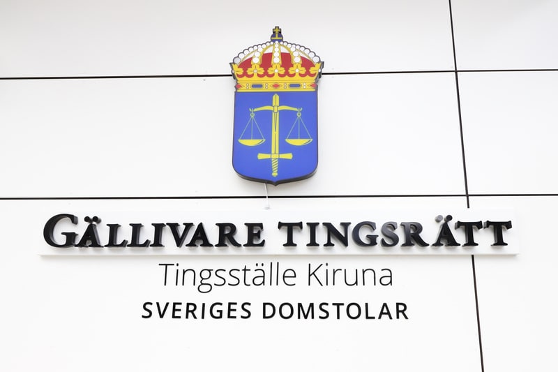 Bilden visar en närbild på en vit skylt med text och en symbol. Överst på skylten, centrerad, sitter en symbol föreställande ett gyllene vågskålsvapen med ett svärd på en blå sköld, toppad med en krona. Under symbolen står texten "GÄLLIVARE TINGSRÄTT