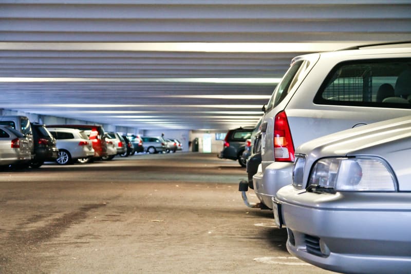 Bilden visar ett underjordiskt parkeringsgarage. I förgrunden till höger syns delar av en ljusgrå bil, troligen en kombi, med fokus på bakre delen av bilen och den högra baklampan. Till vänster om denna bil står en rad med parkerade bilar i olika fär