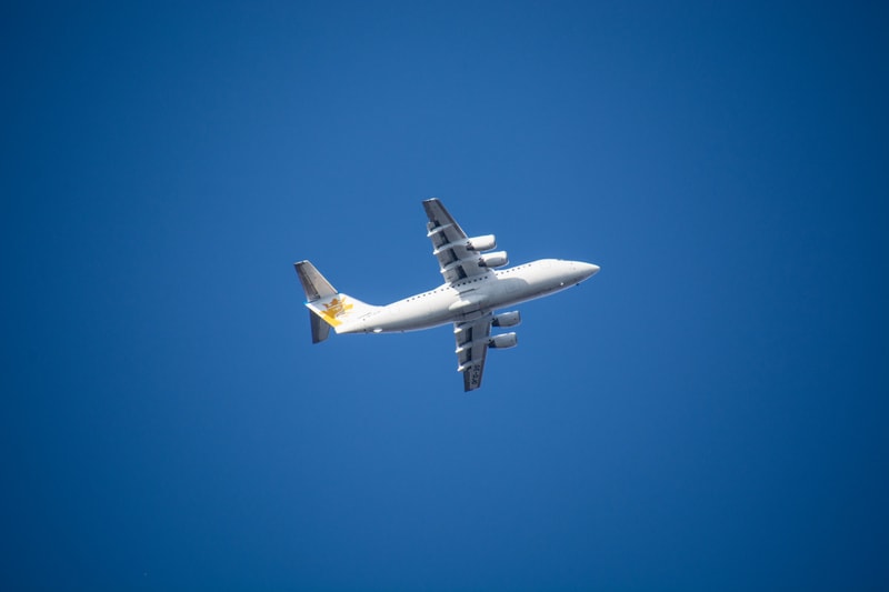 Bilden visar ett flygplan mot en klarblå himmel. Flygplanet är vitt med grå detaljer på vingarna och runt motorerna. På flygplanets fena syns en guldfärgad eller gul logotyp i form av en krona eller liknande symbol. Flygplanet har fyra motorer under
