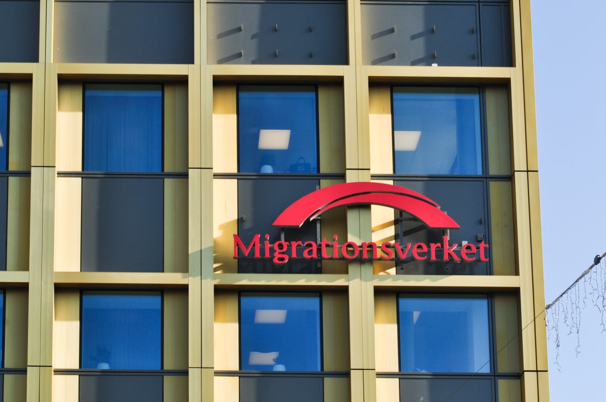 Bilden visar fasaden på en modern byggnad i nära håll. Fastigheten har en guld- eller mässingsfärgad ram som bildar ett rutmönster runt stora, mörkblåa fönster. Mellan fönsterraderna finns mörka paneler. På en av fasadens sektioner, i bildens mitt, s