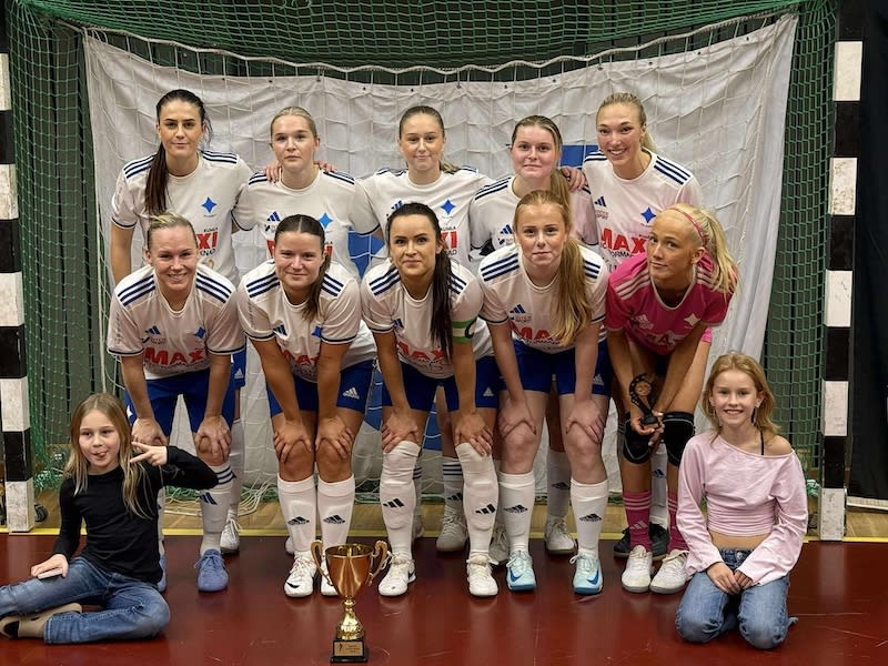 Bilden visar ett lag med elva kvinnor och två flickor i en idrottshall. Nio av kvinnorna är klädda i vita och blåa sportkläder med texten "MAXI ICA KVANTUM ÅFORSOMMAR", medan en kvinna står i en rosa sporttröja med texten "MAXI ICA KVANTUM ÅFORSOMMAR