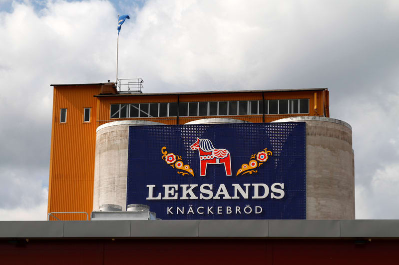 Bilden visar ett gult byggnadskomplex med en stor blå skylt på framsidan. På skylten finns en stiliserad röd dalahäst omgiven av blomsterlika mönster i gult och rött. Under dalahästen står texten "LEKSANDS" med stora vita bokstäver och därunder "KNÄC