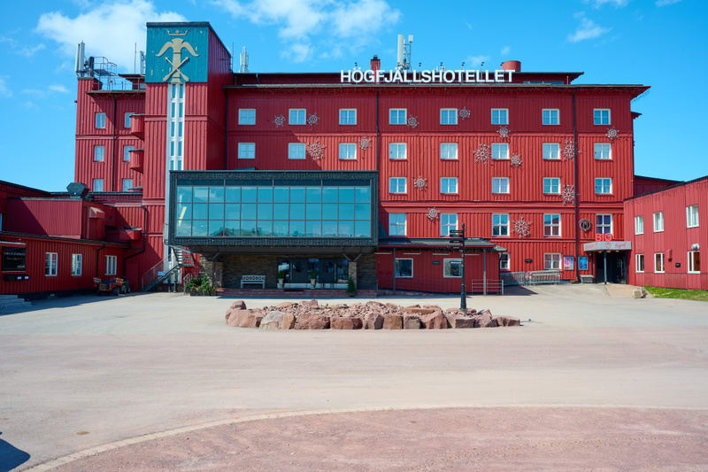 En stor, röd hotellbyggnad med flera våningar och många fönster. Byggnaden är huvudsakligen klädd med röd panel. På taket syns flera antenner eller kommunikationsutrustning. Väggarna är dekorerade med stora snöflingeliknande utsmyckningar. En sektion