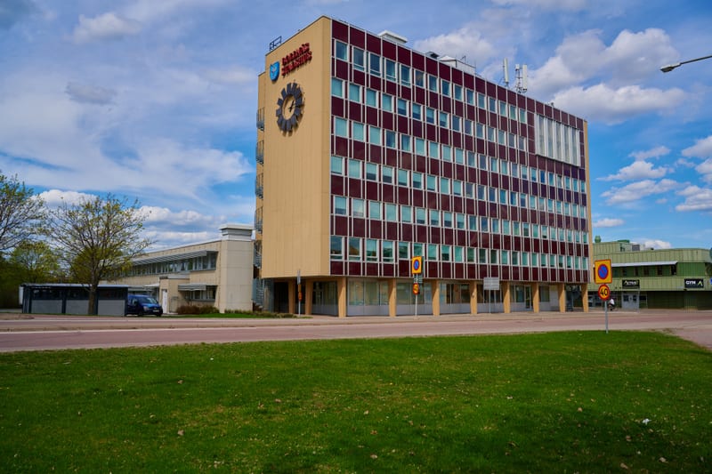 Stadshuset i Bollnäs är en stor byggnad med röd- och beigefärgad fasad. Framför byggnaden finns vägar, gräsytor och trafikskyltar, samt andra byggnader i bakgrunden.