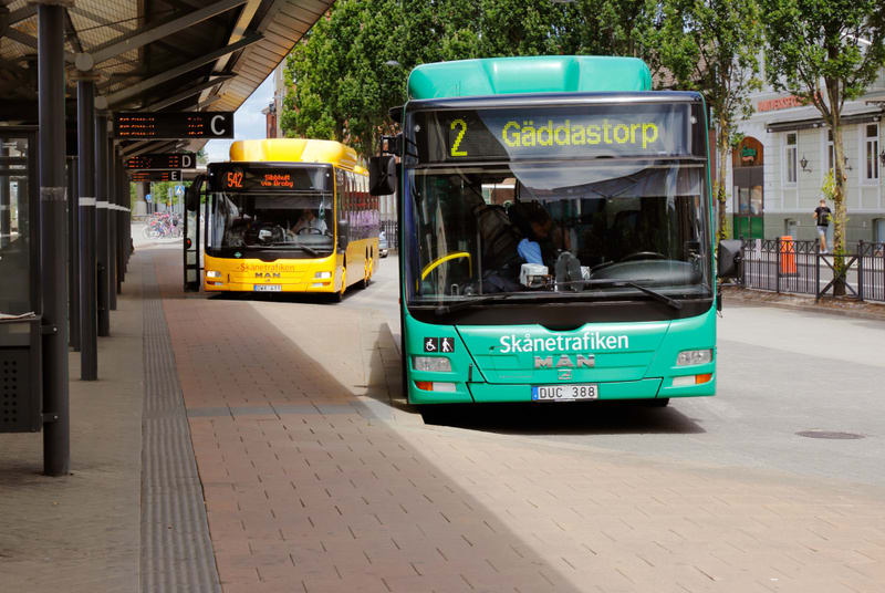 Bilden visar två bussar som står vid en busshållplats under dagtid. En ljusgrön buss står i förgrunden till höger, med texten "Skånetrafiken" och destinationsskylten "2 Gäddastorp" synlig. Bussens registreringsskylt "DUC 388" är också synlig. I bakgr