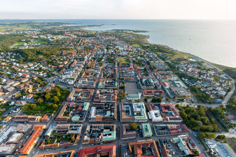 Denna flygfotobild visar en stad sedd uppifrån, centralt belägen vid en kustlinje som sträcker sig längs hela högersidan av bilden. Stadsbebyggelsen består av en blandning av äldre och nyare byggnader med ett rutnät av gator som delar upp staden i kv