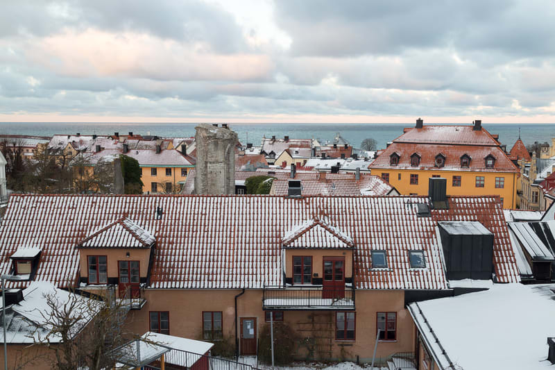 Panoramabild som visar ett stadlandskap med ett flertal byggnader fotograferade uppifrån. Taken på byggnaderna är täckta av ett tunt lager snö, vilket indikerar att det är vinter eller tidig vår. I förgrunden syns taket på en byggnad med terracottarö