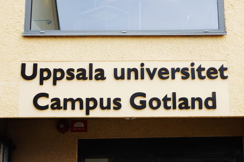 Bilden visar fasaden på en byggnad med en skylt och ett fönster. Skylten sitter på en ljust beigefärgad yta och har svart text som lyder "Uppsala universitet Campus Gotland". Ovanför skylten finns ett fönsterparti med en grå karm. Nedanför skylten, t