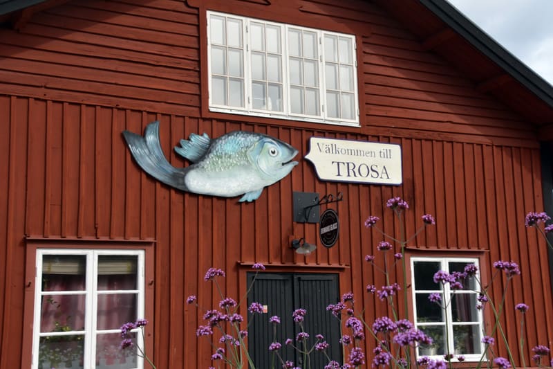 Bilden visar fasaden på en röd träbyggnad med vita fönster. Högst upp i mitten av bilden finns ett stort fönster med åtta rutor. Nedanför fönstret, till vänster, är en väggdekoration formad som en blågrön fisk med öppen mun, vänd mot en skylt där det