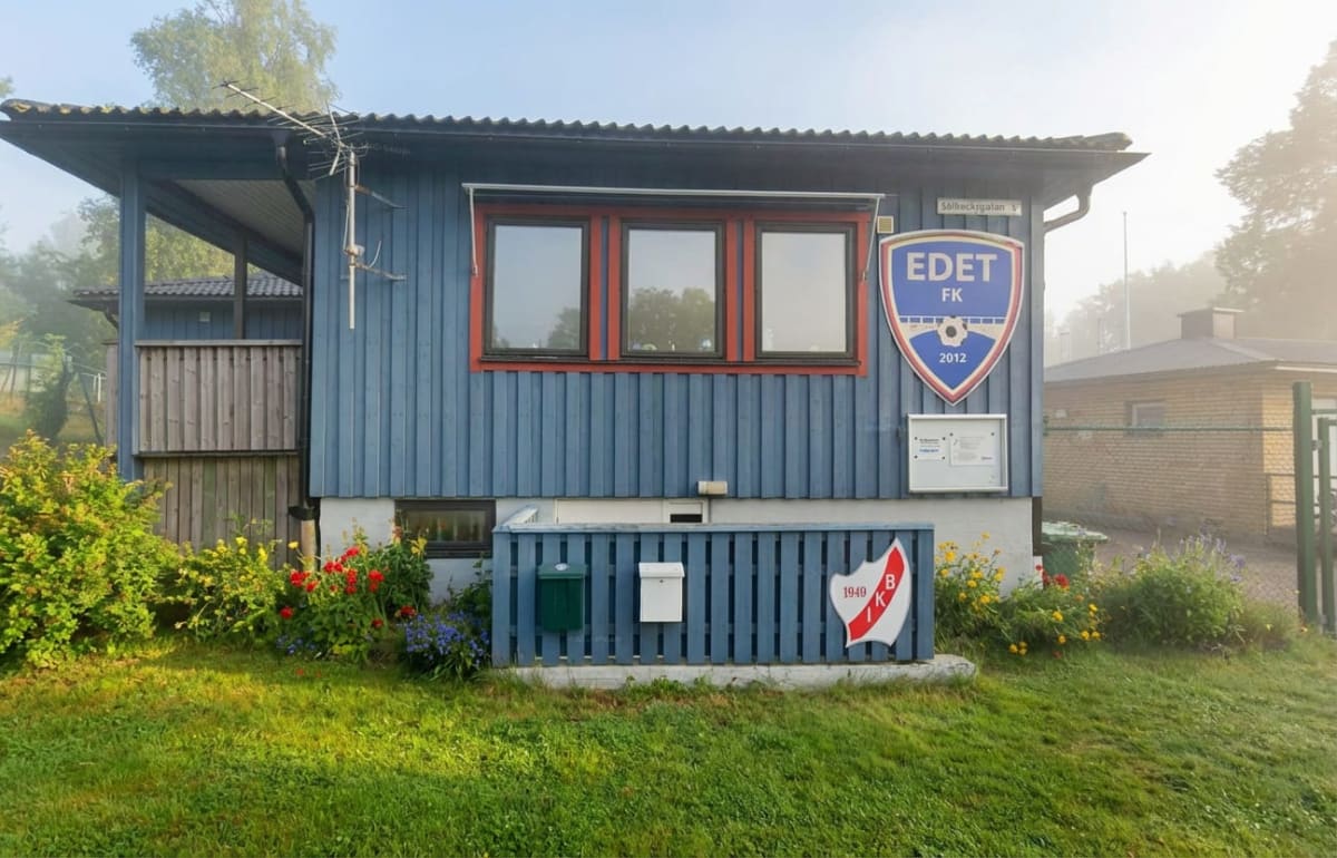 En blåmålad föreningslokal med röda fönsterkarmar och takutsprång. Framför byggnaden finns en grön gräsmatta och blommande buskar. På husväggen sitter en skylt med "EDET FK 2012" och en annan skylt med "BIK 1940".
