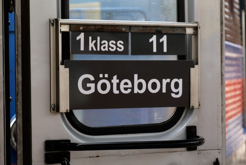 En närbild av en del av utsidan av en tågvagn. Svarta skyltar med vit text "1 klass", "11" och "Göteborg" är fästa på vagnens fönster. Delar av fönstret reflekterar omgivningen.