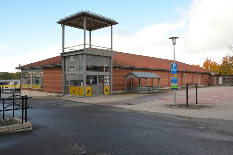 En tegelbyggnad med rött tak och en glaskonstruktion för entré med en utsiktsplattform ovanpå. Framför byggnaden finns en asfalterad yta med en parkeringsskylt och en träkonstruktion med tak. I bakgrunden syns höstlövsbeklädda träd.