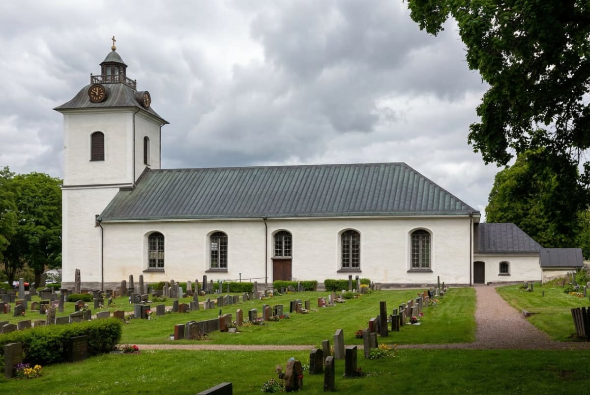 En vit kyrka med en klockstapel och ett grått tak under en molnig himmel. Framför kyrkan finns en gräsmatta med många gravstenar och en grusgång.