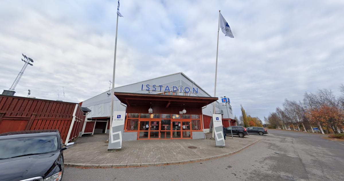 En fasad av en byggnad med texten "ISSTADION" ovanför entrén. Två flaggstänger med flaggor står framför byggnaden. Ett par bilar är parkerade i närheten. Träd med sparsamt lövverk syns i bakgrunden.