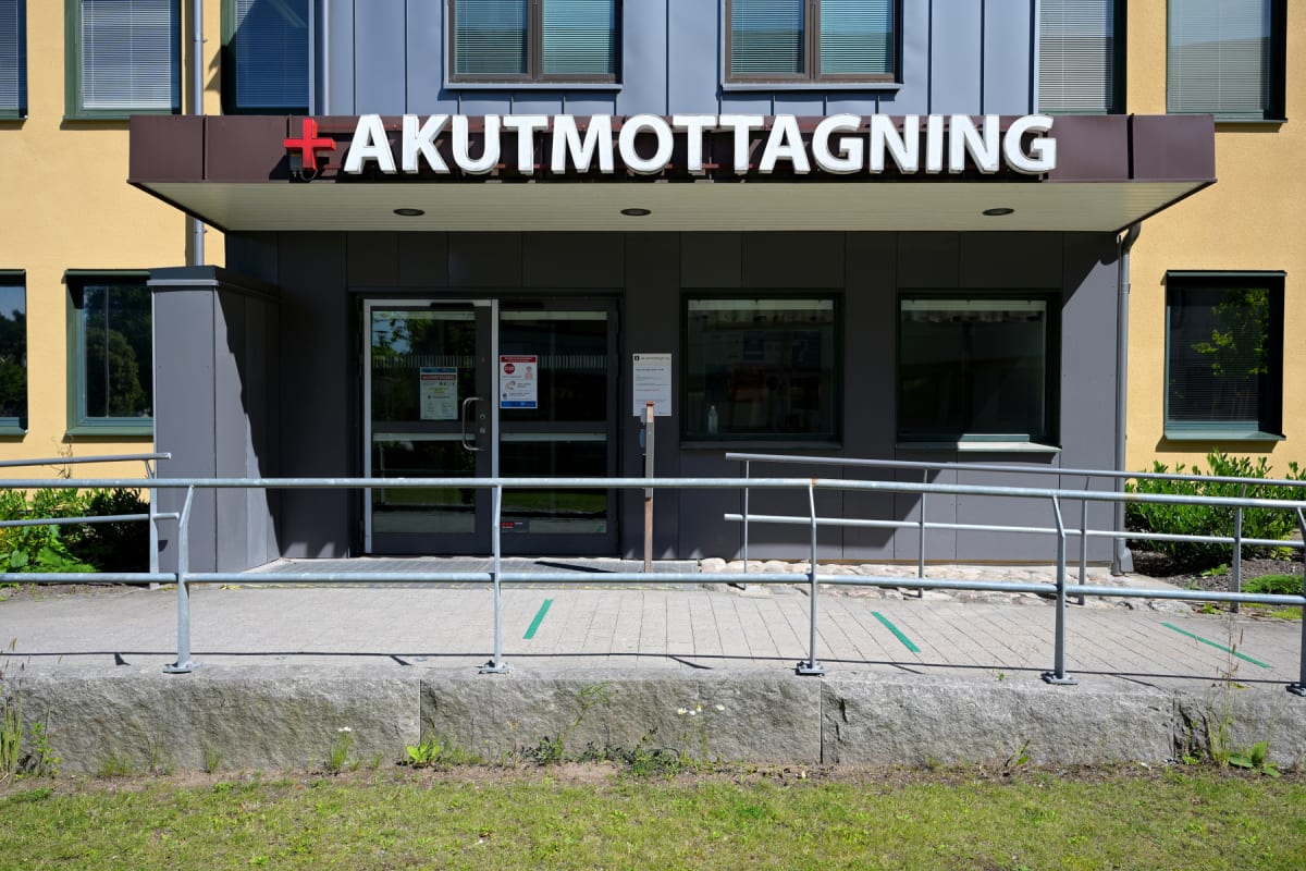 En fasadbild av en akutmottagning i dagsljus. Ovanför entrén står texten "AKUTMOTTAGNING" med ett rött kors. Entrén har en trappa och en ramp med räcken. På dörrarna och i fönstren bredvid dem syns anslag. Fasaden är ljusgul och grå med fönster.
