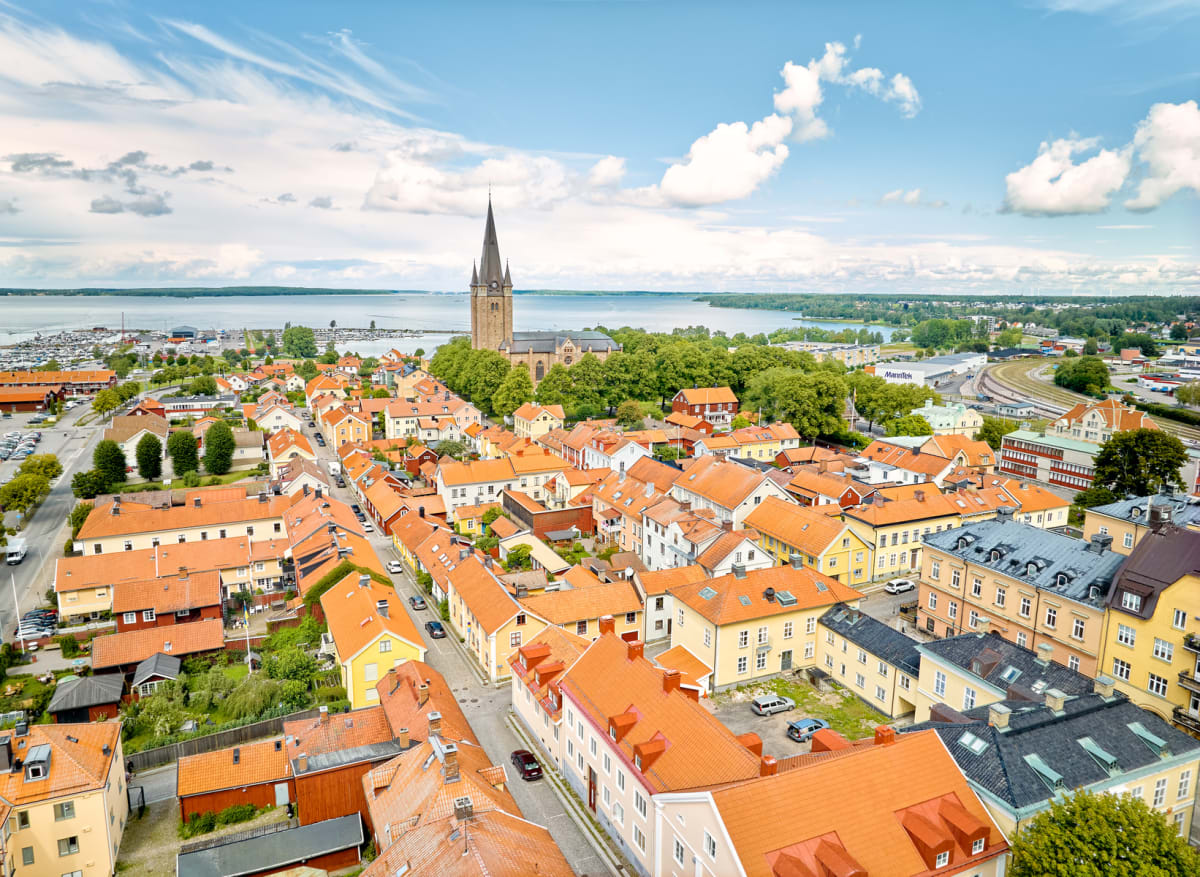 En vidvinkelbild tagen uppifrån visar en stad med många byggnader med röda tak, i förgrunden av en stor sjö med en småbåtshamn. En stor kyrkobyggnad med en spetsig spira är synlig något till vänster om mitten.