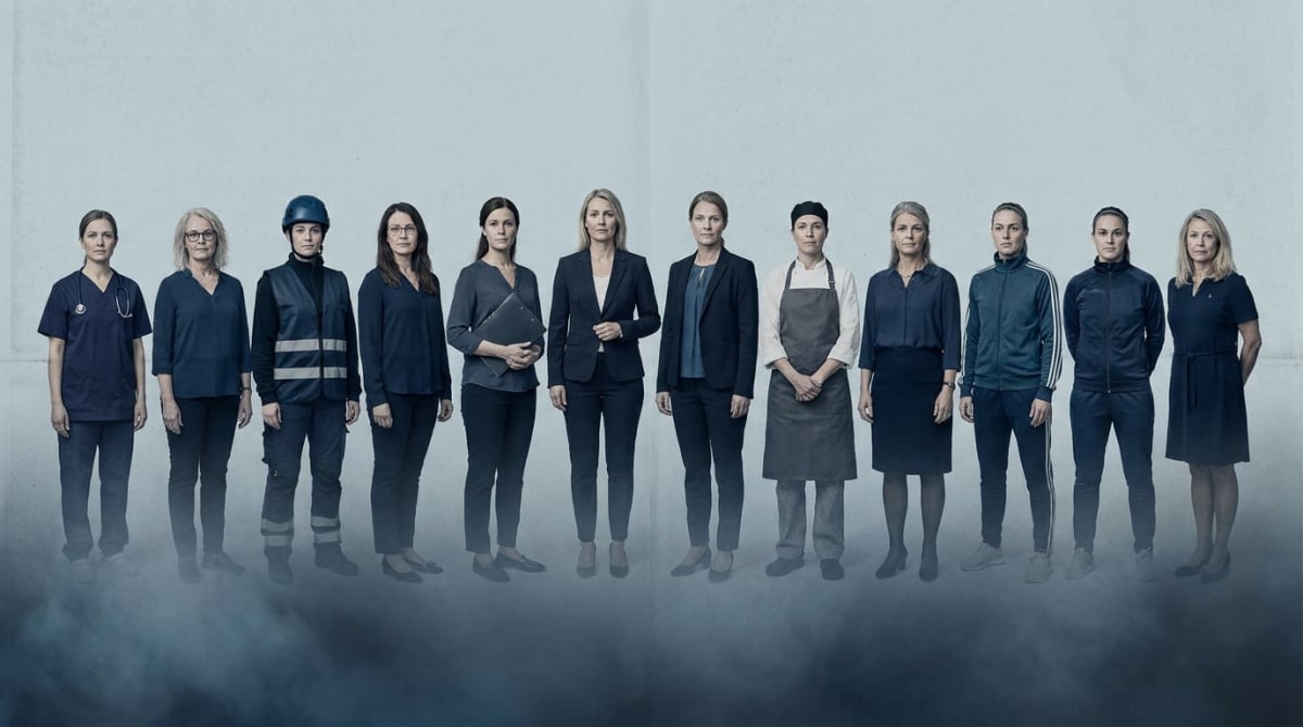 Bilden visar elva kvinnor i olika yrkeskläder stående på rad mot en ljusgrå bakgrund, med dimma vid fötterna. Deras ansikten har ett neutralt uttryck.
