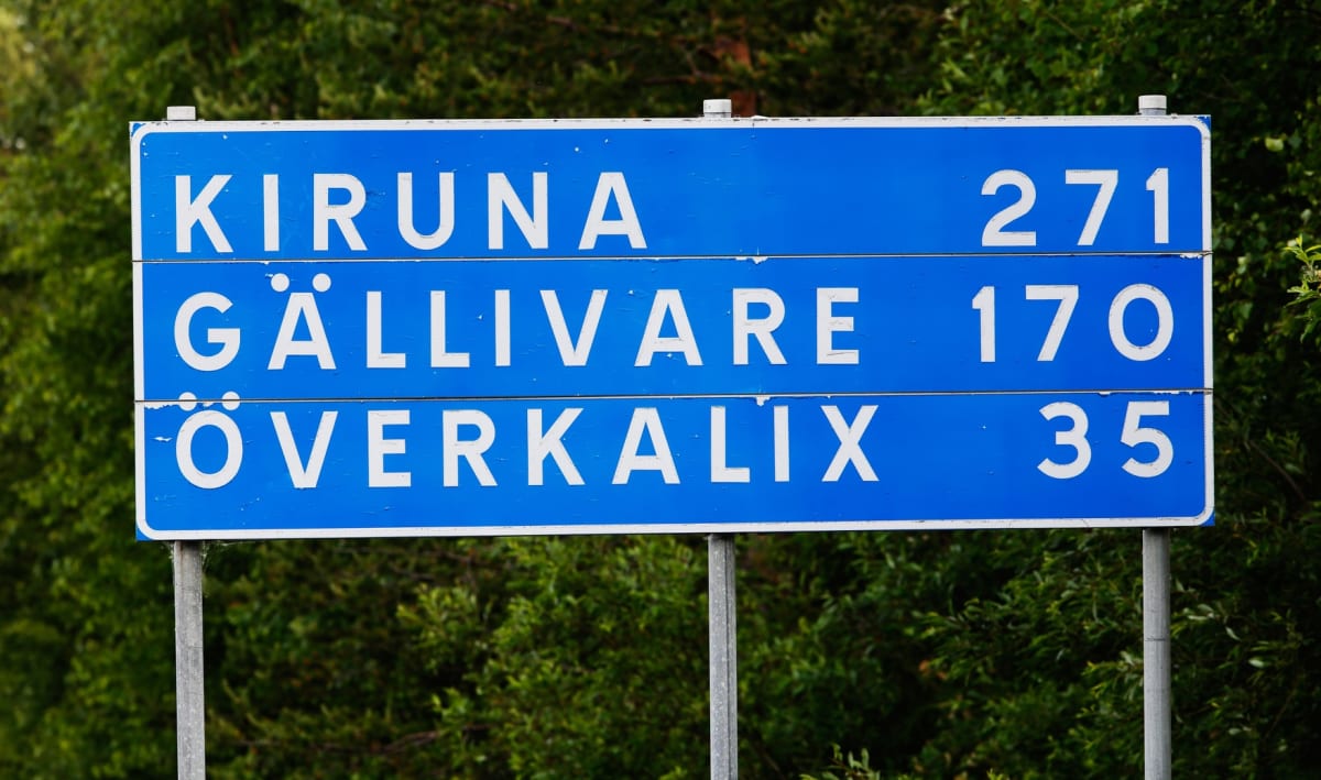 En blå vägskylt med vita bokstäver visar avstånd till Kiruna (271), Gällivare (170) och Överkalix (35). Skylten är monterad på två silverfärgade stolpar och i bakgrunden syns grön växtlighet.