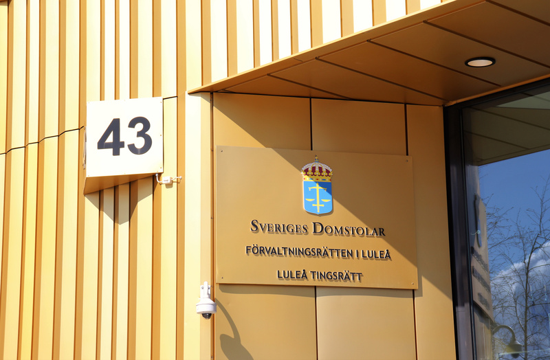 Bilden visar fasaden på en byggnad med en husnummerplåt och en skylt. Husnummerplåten är vit med svart text "43". Skylten är guldfärgad med texten "SVERIGES DOMSTOLAR FÖRVALTNINGSRÄTTEN I LULEÅ LULEÅ TINGSRÄTT" och har Sveriges riksvapen med tre kron