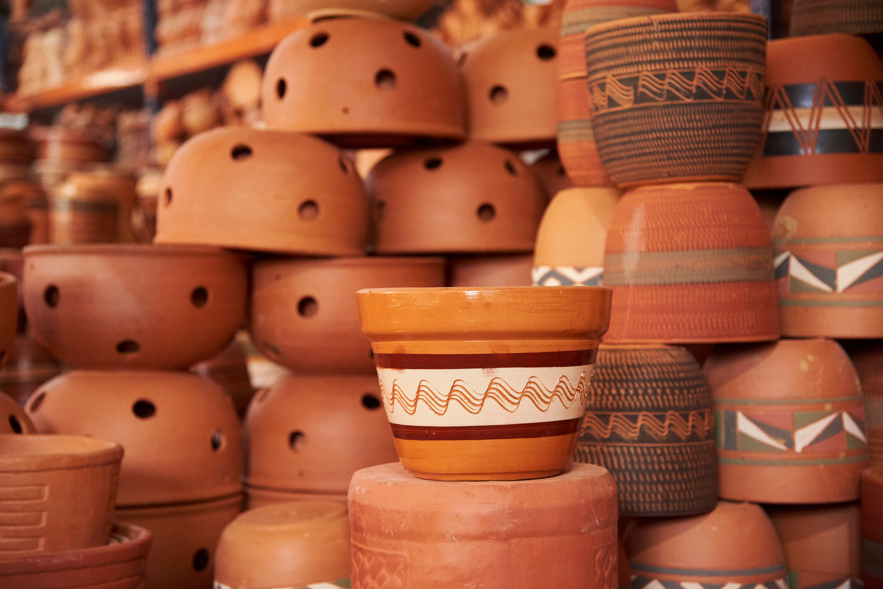En bild som visar en stor samling av terrakottakrukor och lerkärl i olika former och storlekar. En del av kärlen har målade mönster, andra är enfärgade i rödbruna nyanser, och några har hål. Det finns olika typs av prydnadsföremål.