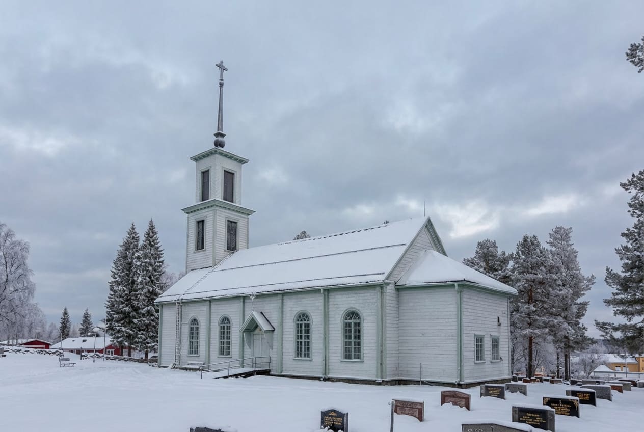 En vit träkyrka står i ett snötäckt landskap under en molnig himmel. Kyrkan har ett högt torn med ett kors på toppen, och dess tak är täckt av snö. I förgrunden syns snötäckta gravstenar, och i bakgrunden finns snötyngda träd och enstaka byggnader.