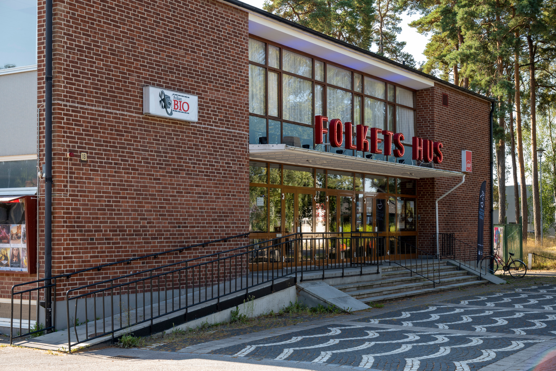 En fasad av ett hus med tegelväggar och stora fönsterpartier. På fasaden syns texten "FOLKETS HUS" i rött neonljus och en skylt med texten "Folkan BIO". En svart cykel står parkerad intill byggnaden.