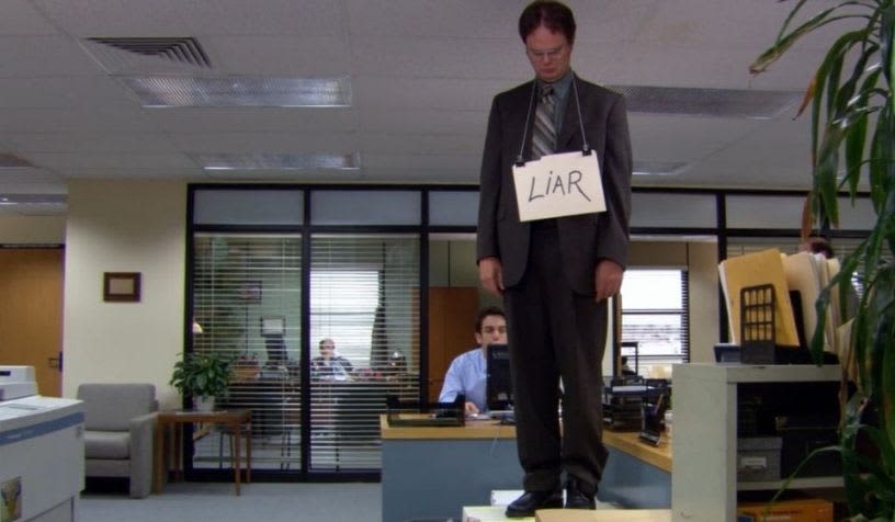 dwight standing on a table with a liar card around his neck