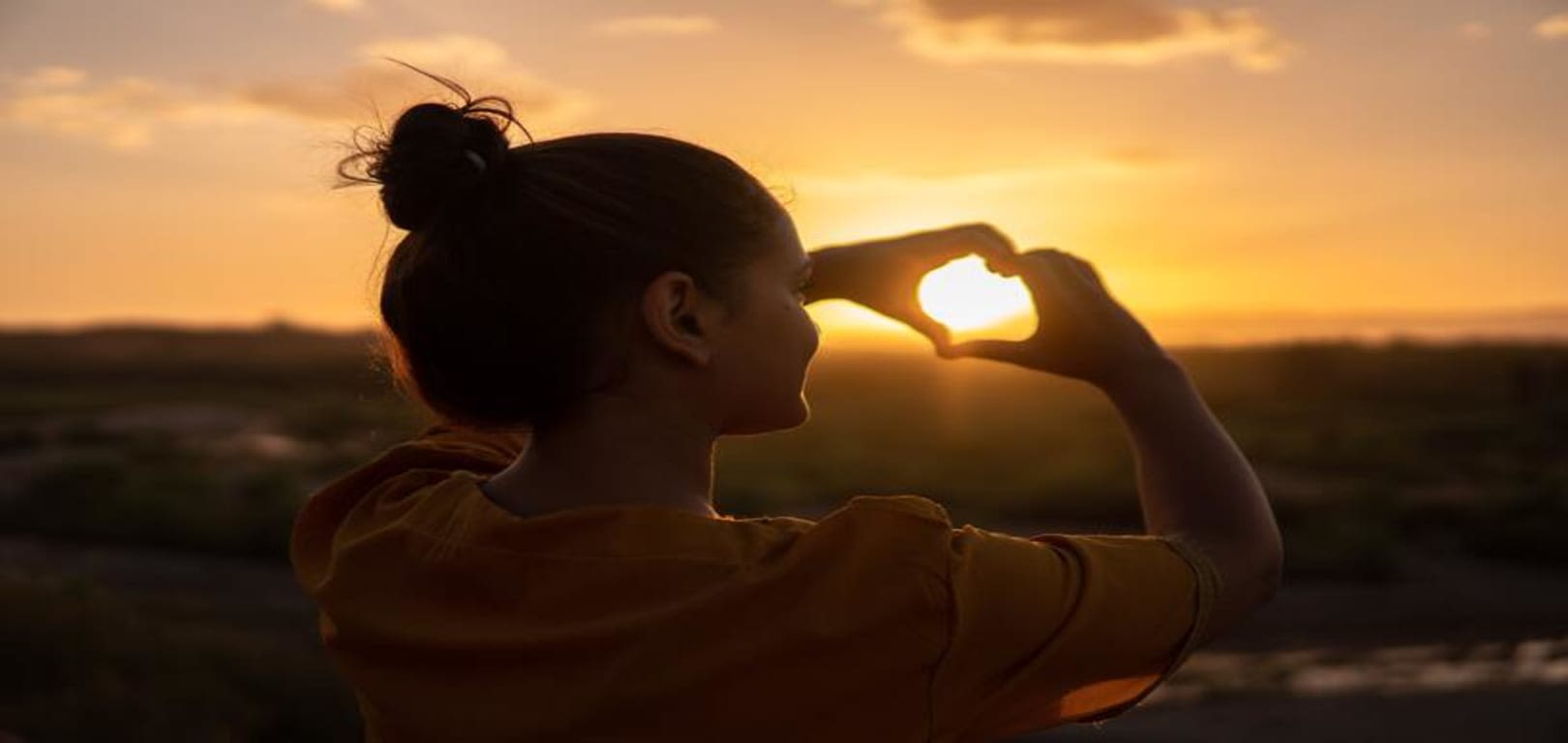 image of a woman holding heart at the sun with her hands