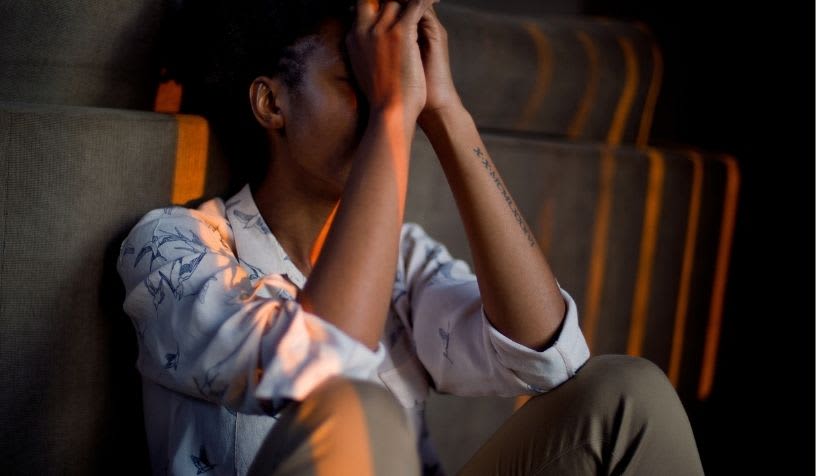 person of gender unknown sitting on the floor with hands covering their face