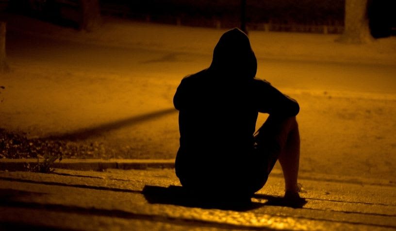 man in a hoodie sitting on a dark dimly lit street