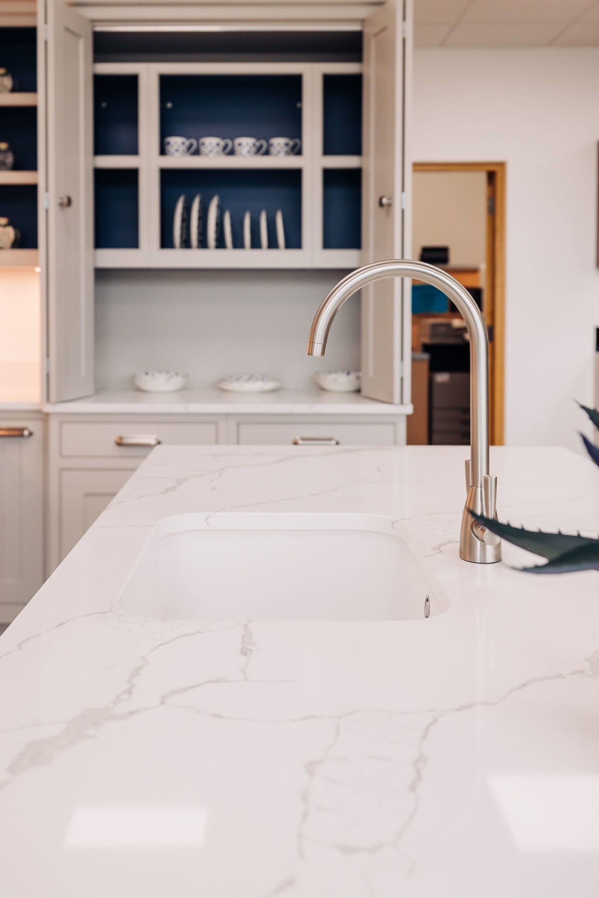 A marble quartz worktop in white with vein runnignthrough it, with a larder open in the background