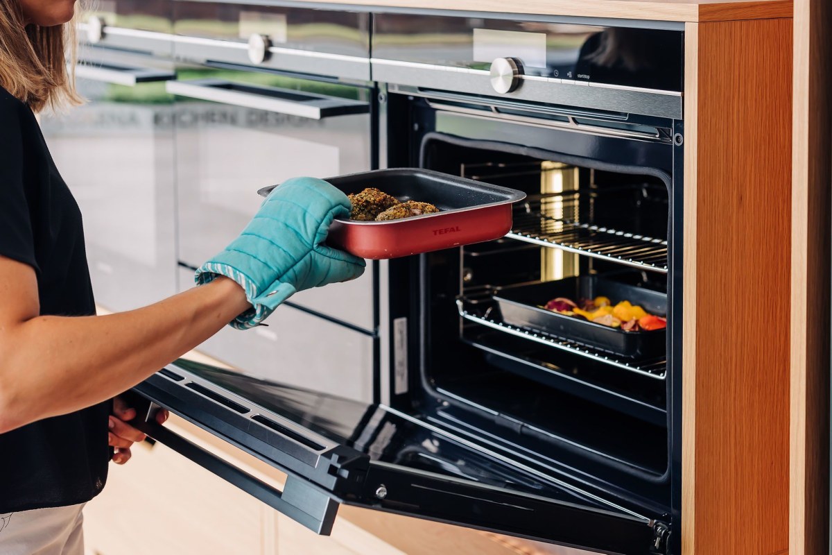 A hand removes an oven dish from a Neff Slide&Hide oven in a bank of ovens