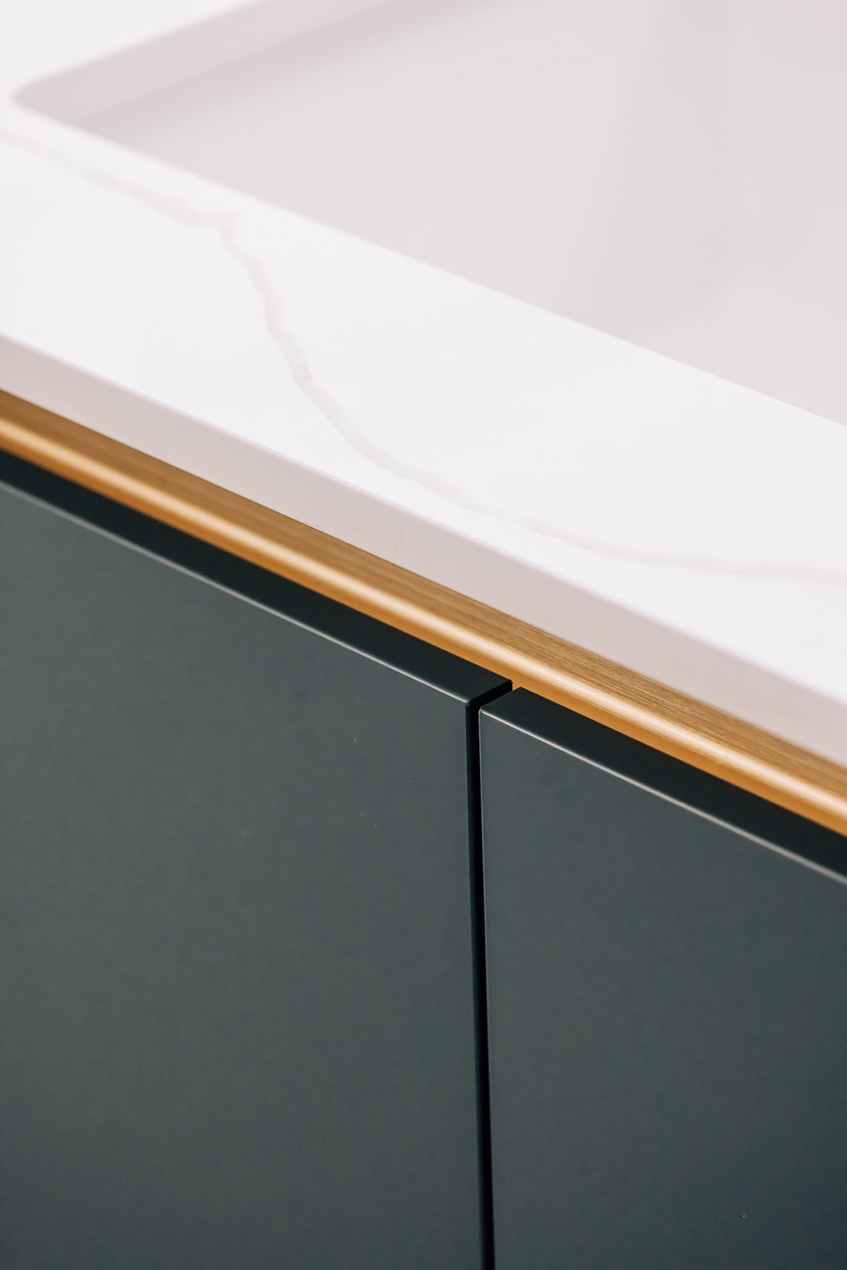 A close up of blue handleless cabinetry, with gold rail and white quartz worktops