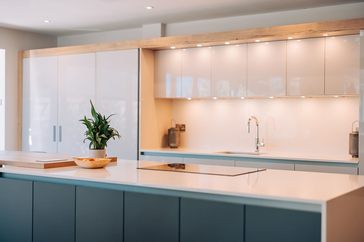 A Modern kitchen island with white quartz worktop, blue cabinetry and white gloss cabinetry behind