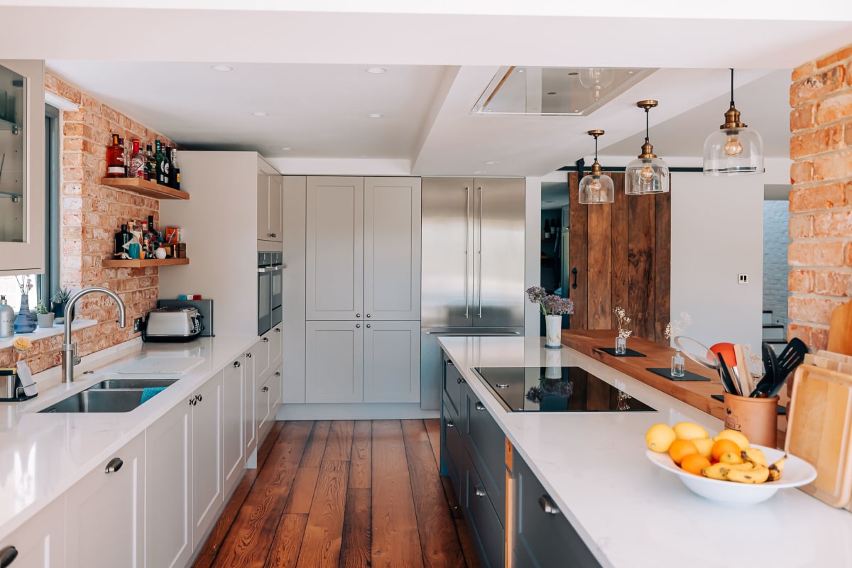 An indisutrial Kitchen with wooden floors, steel fridge, white worktops