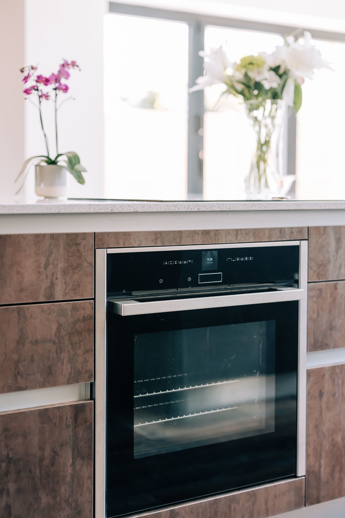 A neff slide and hide oven in a kitchen island with oxidised amber cupboards