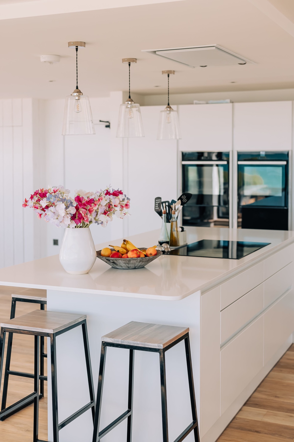 A kitchen island with white units, white quartz worktops and two metal and wood bar stools